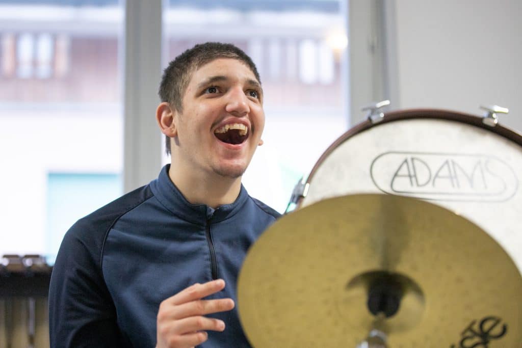 Ragazzo che sorride mentre partecipa a una sessione di MusicoTerapia Orchestrale, suonando strumenti a percussione.