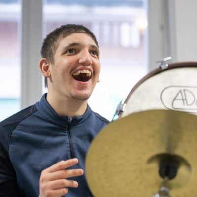 Ragazzo che sorride mentre partecipa a una sessione di MusicoTerapia Orchestrale, suonando strumenti a percussione.