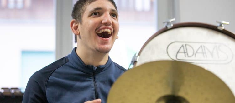 Ragazzo che sorride mentre partecipa a una sessione di MusicoTerapia Orchestrale, suonando strumenti a percussione.